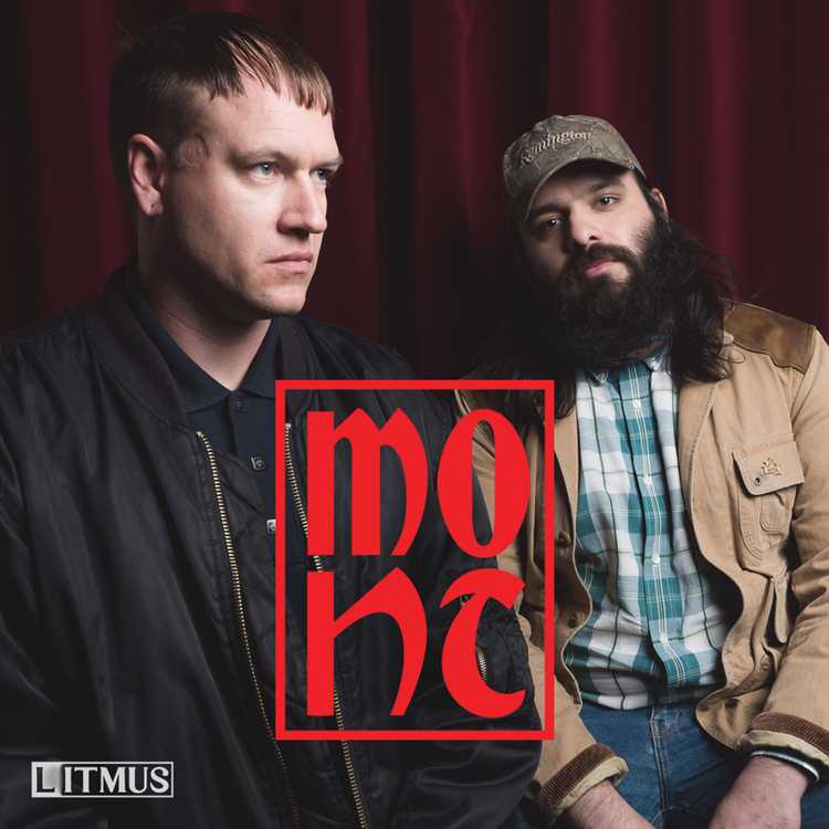 Mont Icons cover tile which is a photo of the hosts Daniel Stewart and Mahmood Fazal. They are sitting next to each other, unsmiling. Daniel is on the left, wearing a black shirt and jacket. Mahmood is on the right wearing a hunting cap, beige shirt, checkered shirt and jeans. The Mont logo is large and red and is on top of the image. Behind them is a dark red velvet curtain.